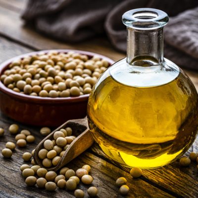 Close up view of a glass bottle filled with soy oil shot on rustic wooden table. A bowl with dried soybeand complete the composition Plant-based nutrition concept. High resolution 42Mp studio digital capture taken with Sony A7rII and Sony FE 90mm f2.8 macro G OSS lens